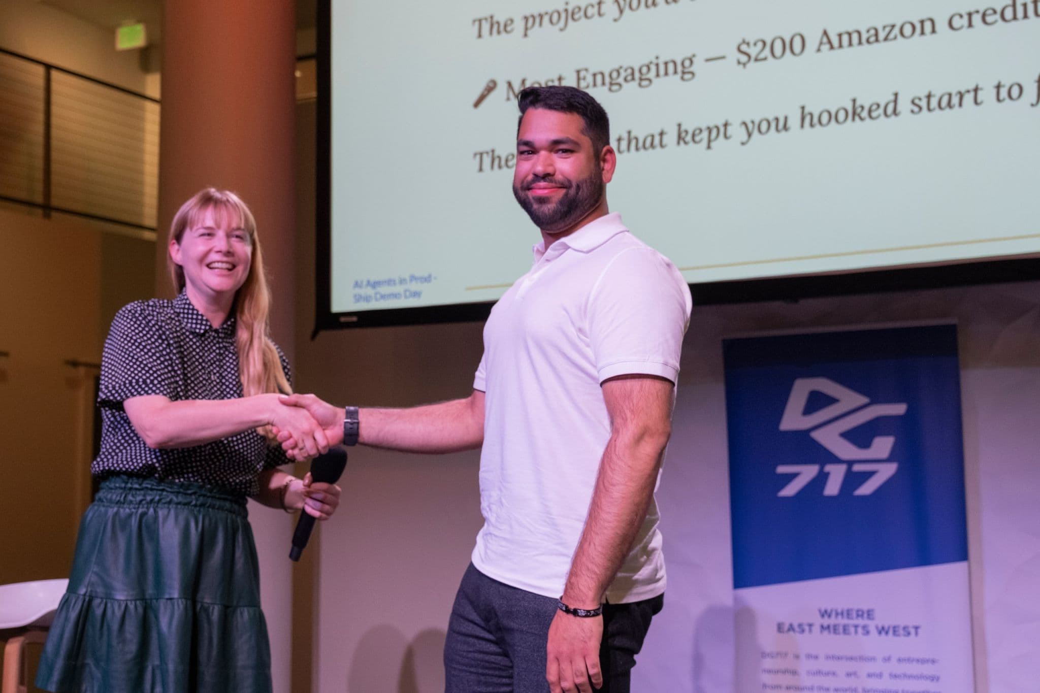 A prize winner shaking hands after presenting a project on stage.